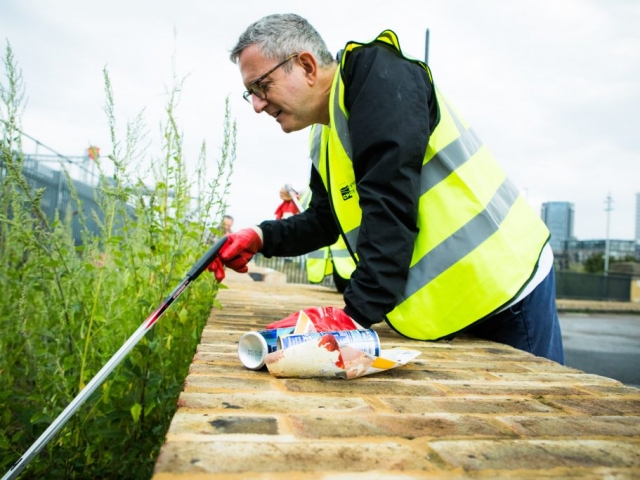 Man leaning over wall picking litter with rubbish on wall with tower blocks in background